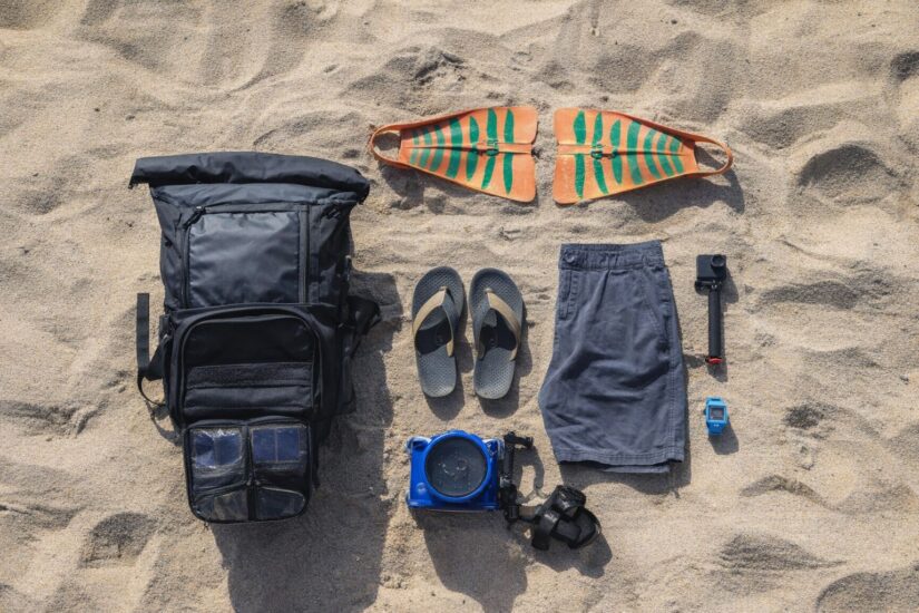 Reseutrustning och strandprylar utlagda på sand.