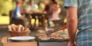 Person grillar kött utomhus medan familjen sitter vid ett bord