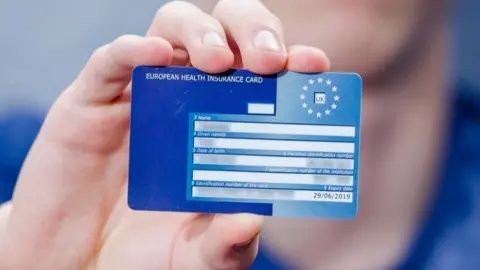 Hand som håller upp ett blått europeiskt sjukförsäkringskort